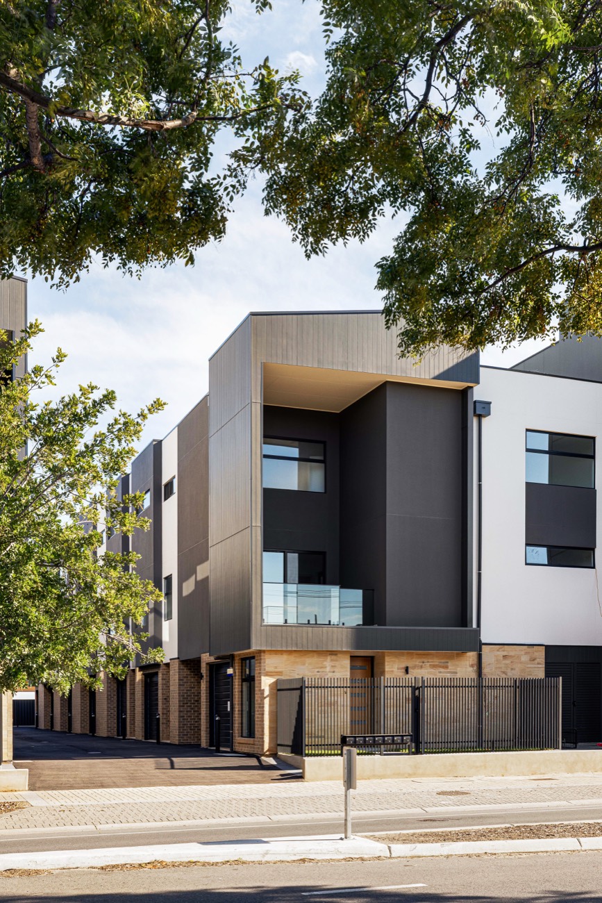 A completed residential building, seen from the street through street trees.
